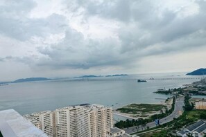 A coastal cityscape with high-rise buildings, a bridge, and a body of water under cloudy skies. - Ocean Home@Urban Suites@3BR@10+2 Pax (Jelutong)