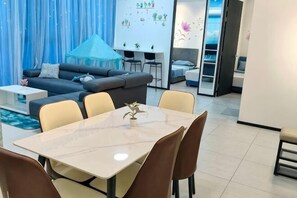 A modern living room with a sofa, dining table, chairs, and a kitchen area. - Ocean Home@Urban Suites@3BR@10+2 Pax (Jelutong)