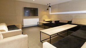 Ein modernes Wohnzimmer mit einer Couch, Sesseln, einem Couchtisch und einem an der Wand befestigten Flachbildfernseher.