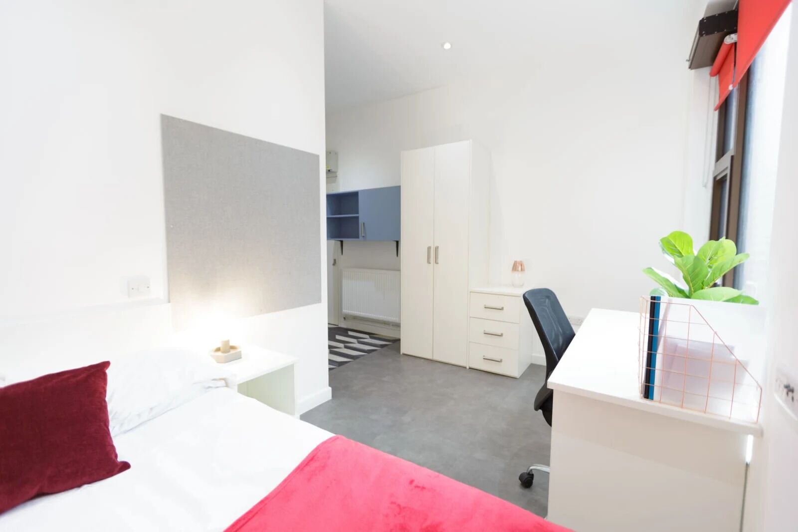Una habitación de hotel con una cama, un escritorio, una silla, un radiador y una ventana con cortinas.
