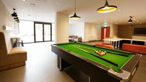 Ein moderner, überdachter Billardtisch mit grüner Spielbahn, umgeben von Sitzbereichen und Pendelleuchten.
