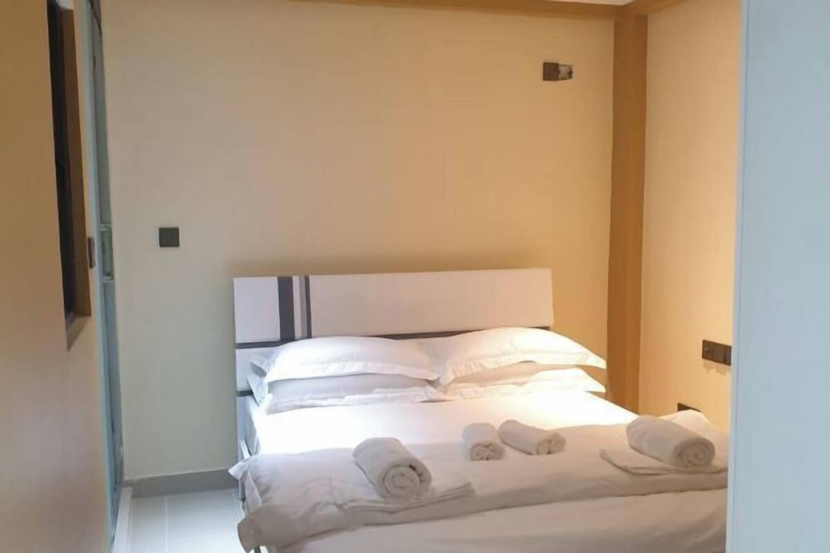 A hotel room with a bed, pillows, and rolled towels.
