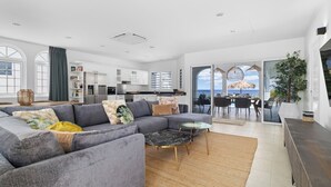 A modern living area with a grey sectional sofa, a round coffee table, and a kitchen in the background. - Stunning Oceanfront Vacation Villa with Private Pool and Beach Access (Kralendijk)