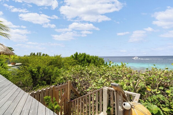 A wooden deck with a view of the ocean and a boat in the distance. - Stunning Oceanfront Vacation Villa with Private Pool and Beach Access (Kralendijk)