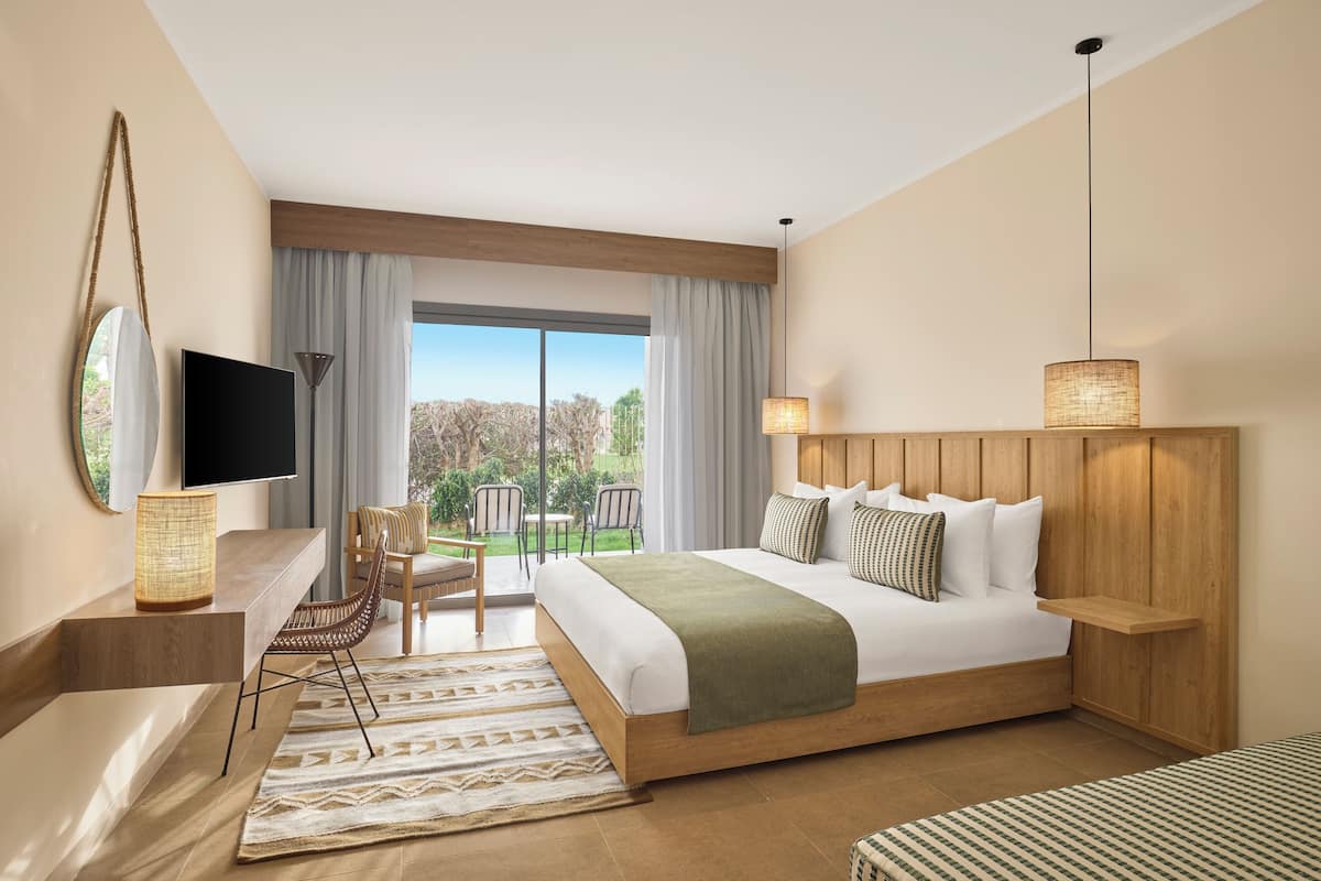 A modern hotel room with a large bed, a TV, a desk with a chair, and a view of the outdoors.