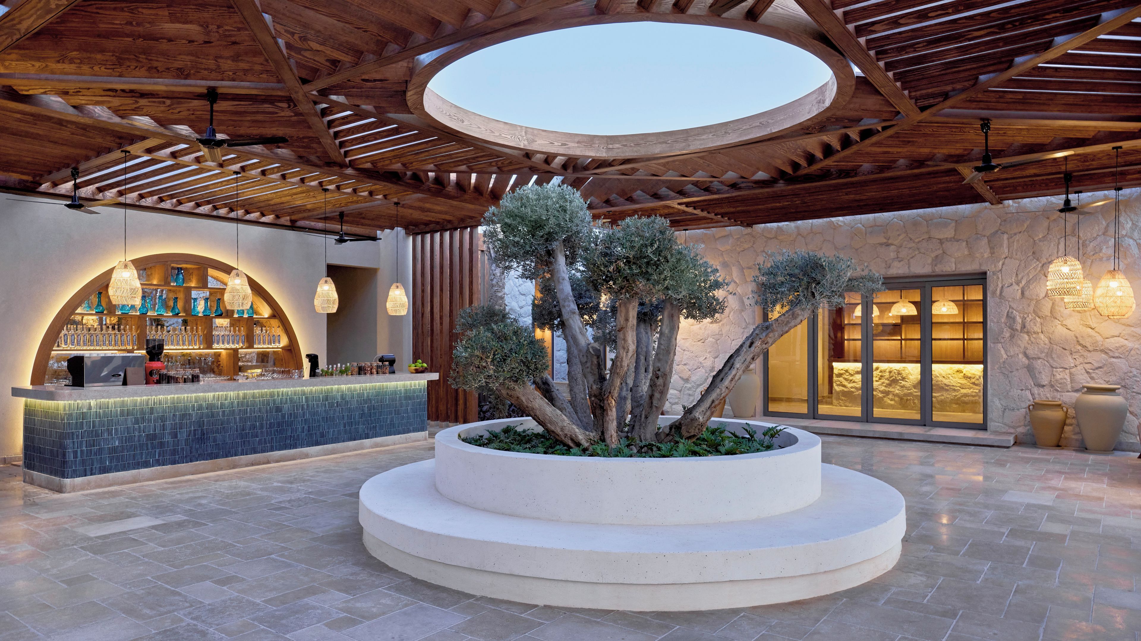 A bar area with a circular seating arrangement, a stone wall, and a wooden ceiling structure.