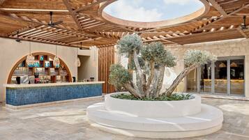 A covered outdoor area with a central planter with trees, a bar area with blue-tiled counter, and a wooden ceiling structure.