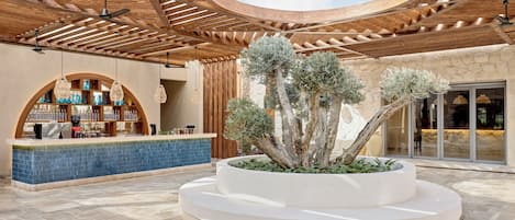 A covered outdoor area with a central planter with trees, a bar area with blue-tiled counter, and a wooden ceiling structure.