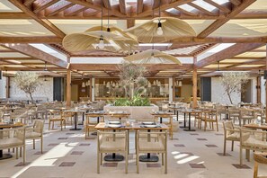 A spacious indoor dining area with wooden tables and chairs, a central plant arrangement, and a high wooden ceiling with natural light. - JAZ Viva Almaza Blu, Almaza Bay (Marsa Matrouh)