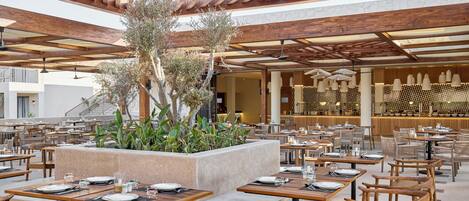 An outdoor dining area with wooden tables and benches, a central planter with greenery, and a modern interior with patterned wall decor.