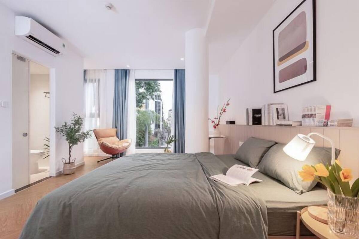A modern hotel room with a bed, a chair, a desk, a lamp, and a view of the outdoors.