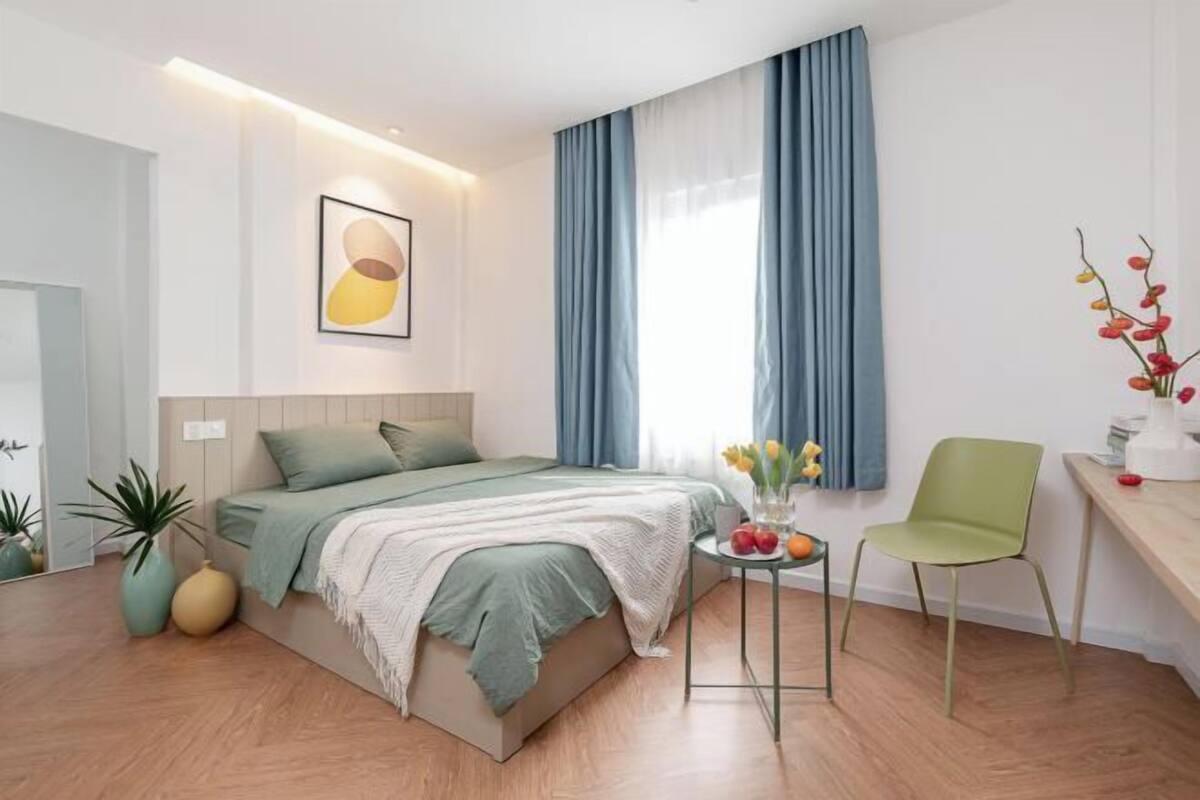 A modern bedroom with a bed, a small table with flowers, a chair, and a desk.