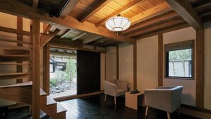 A room with a wooden ceiling, a staircase, a chair, a small table, and a window. - RICKA KATSUURA (Katsuura)