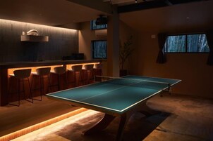 A room with a ping pong table, bar stools, and a bar area.