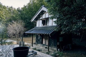 Un edificio de estilo japonés tradicional con techo de tejas y estructura de madera, rodeado de vegetación.