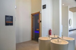A modern bathroom with three sinks, a mirror, and a door leading to a shower area.