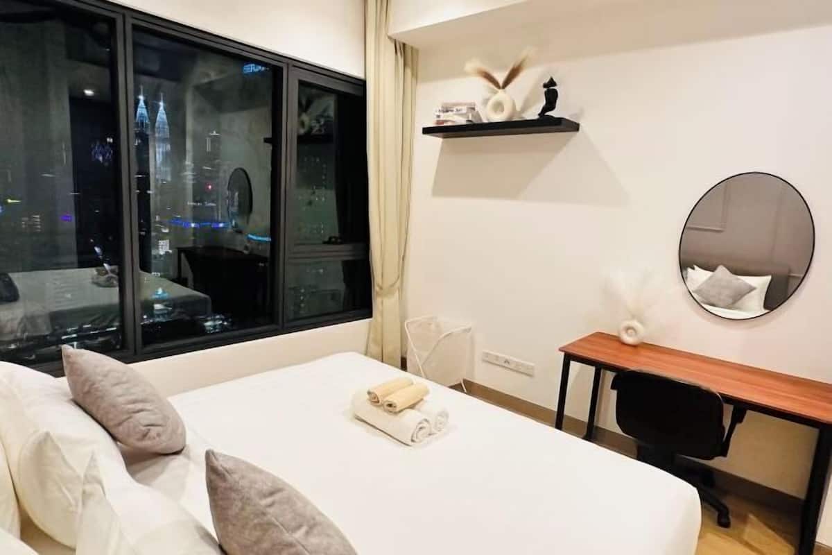 Una habitación de hotel con cama, escritorio, silla, espejo y ventana con vista a la ciudad.