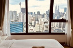 Une chambre d’hôtel dotée d’une grande fenêtre donnant sur le paysage urbain, d’un lit recouvert d’une courtepointe à rayures et d’un rebord de fenêtre orné d’un petit objet.