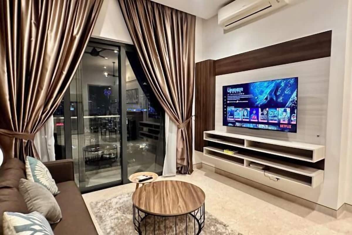Una sala de estar moderna con un televisor de pantalla plana, un sofá, una mesa de centro y un ventanal corredero que da a un balcón.
