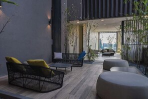Ein moderner Außenbereich mit einer Couch, Sesseln und Hocker, umgeben von Bambuspflanzen und Blick auf die Stadt.
