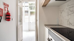 Une cuisine moderne avec un poêle noir, un dosseret en marbre blanc et une porte en verre donnant sur une pièce lumineuse.