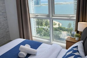 A hotel room with a bed, a nightstand with a lamp, a framed photo, and a view of a coastal area. - HappySty in George Town Amazing sea view (George Town)