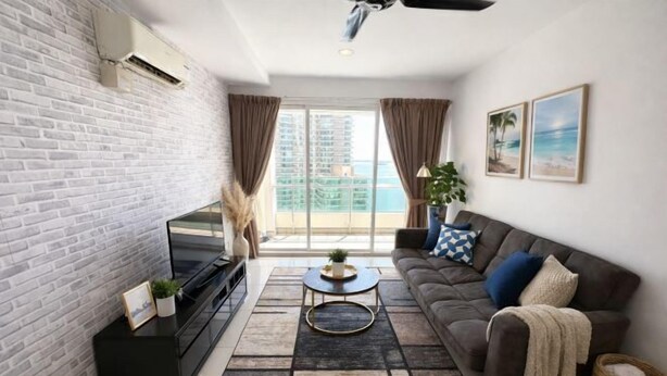 A modern living room with a brick wall, a flat-screen TV, a sofa with cushions, a coffee table, and a view of a balcony with a cityscape. - HappySty in George Town Amazing sea view (George Town)