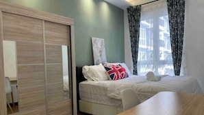 A bedroom with a bed, a wooden table, a sliding door, and a window with curtains. - Elevated Cozy Homestay @Heart of Sri Petaling 3R3B (Kuala Lumpur)