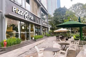 Un espace extérieur aménagé avec des tables et des chaises, une enseigne indiquant qu’il s’agit d’un pub servant des pizzas, et un parasol vert.