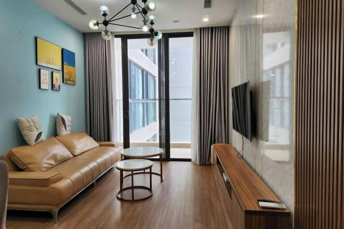Un salon moderne avec un canapé en cuir marron, deux petites tables rondes, un banc en bois et un téléviseur à écran plat fixé au mur.