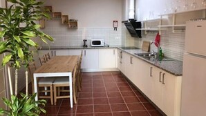 Une cuisine de taille réduite avec des meubles blancs, une table à manger en bois et un sol carrelé.