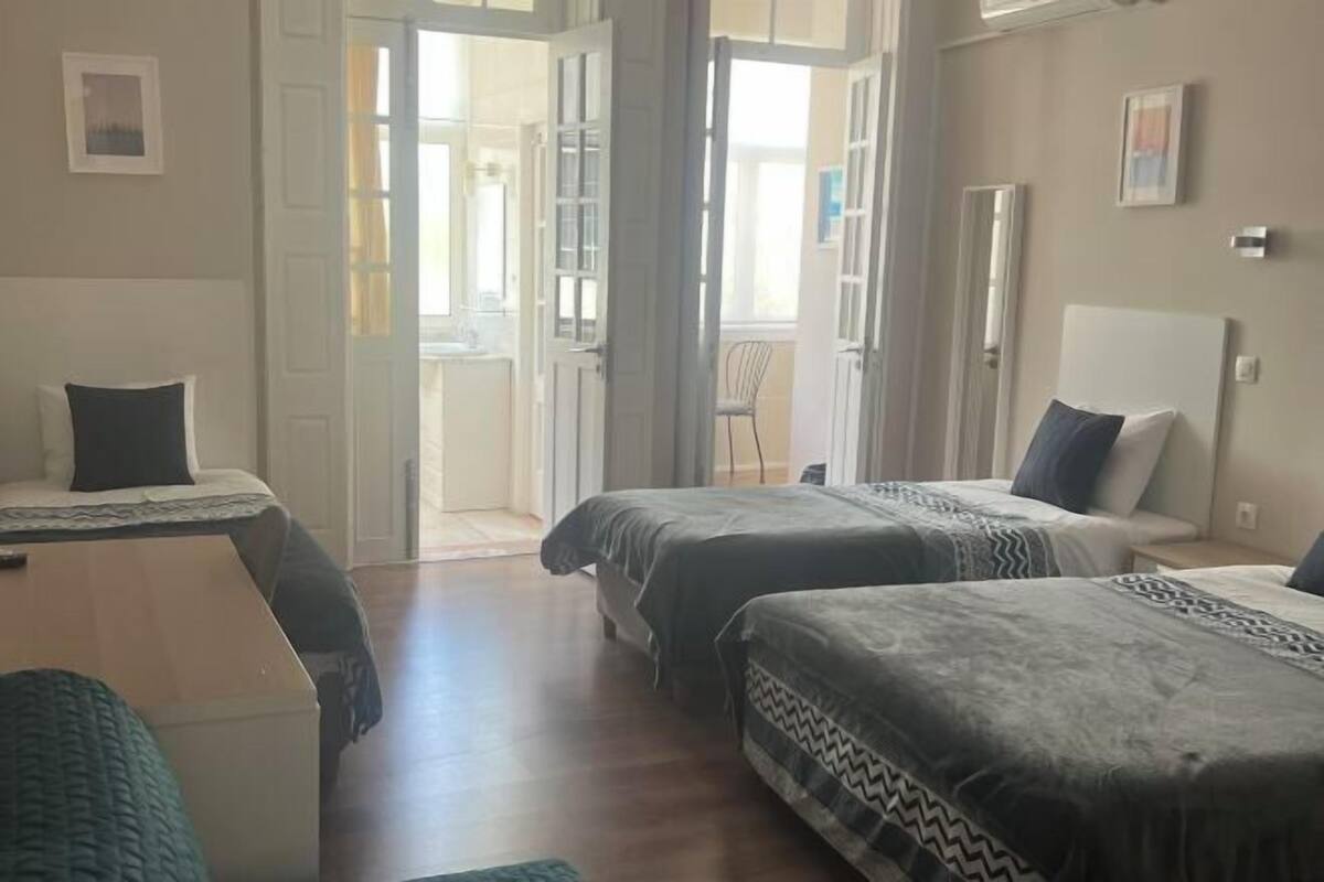 A hotel room with two beds, a small table, and a chair. There are doors leading to a balcony.