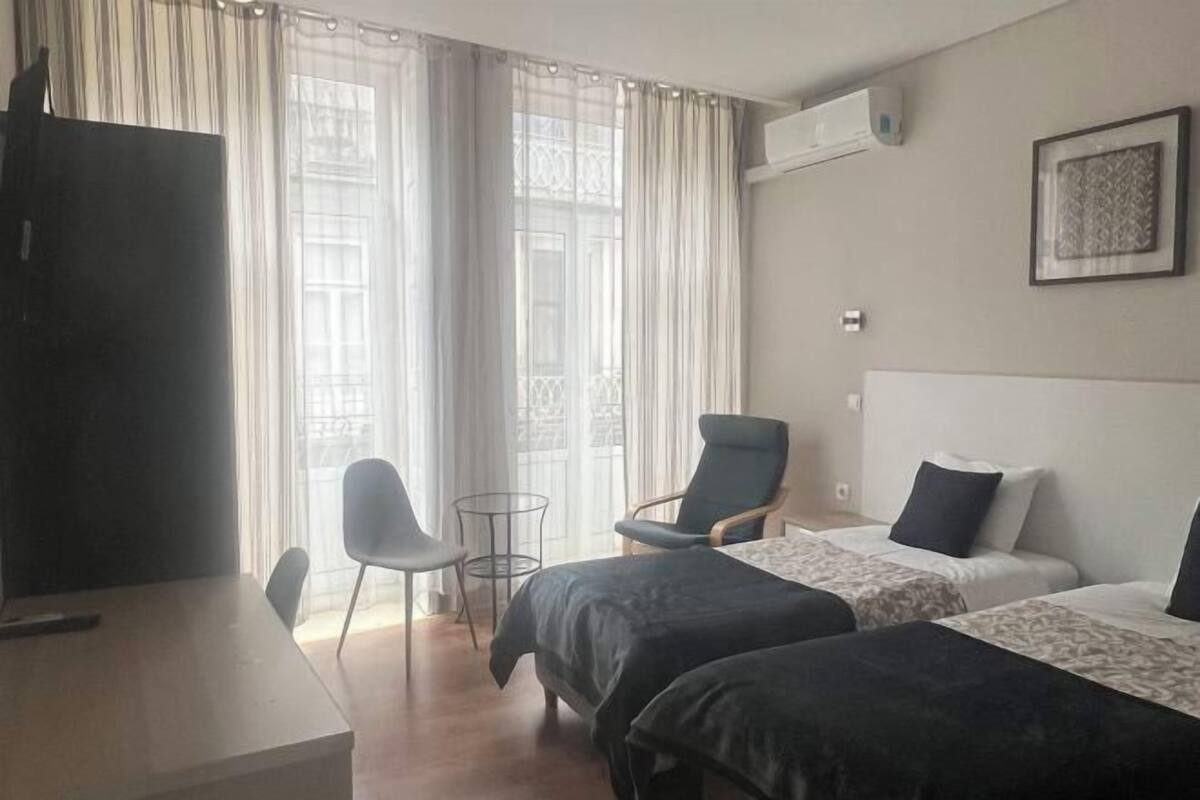 A hotel room with two beds, a desk, a chair, and a TV.