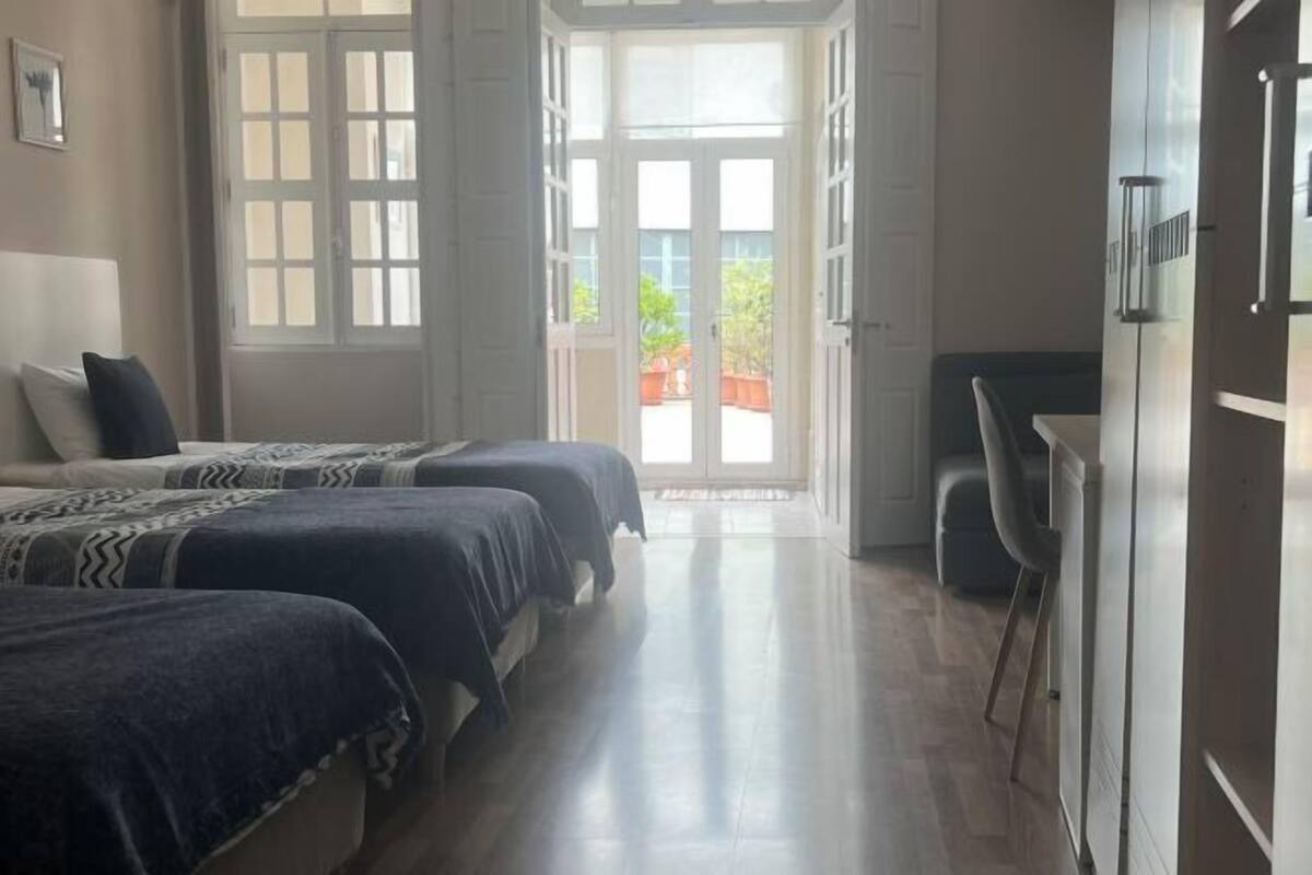 A room with two beds, a desk, and a door leading to a balcony.