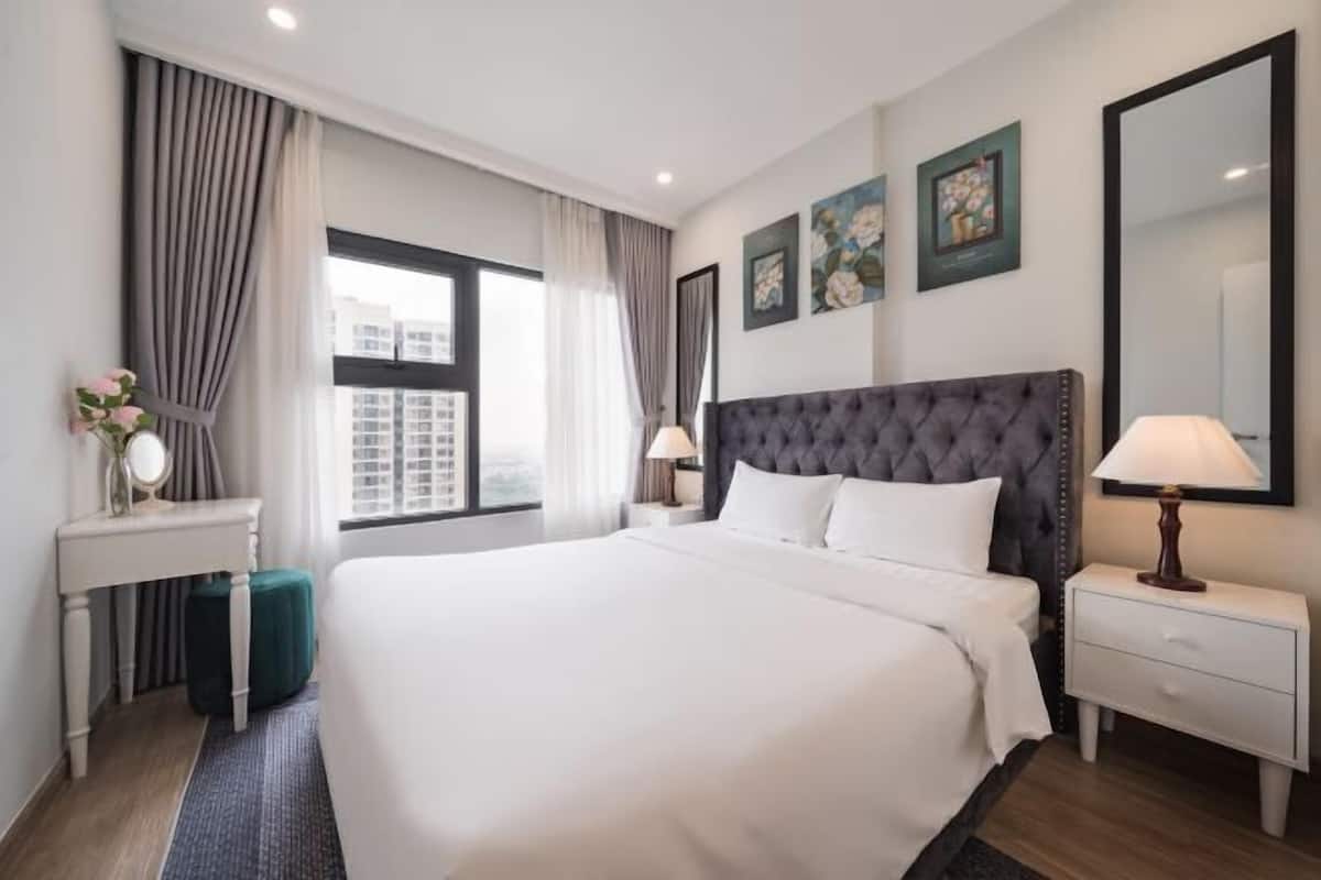 Une chambre d’hôtel avec un grand lit, des tables de chevet, une fenêtre avec des rideaux et des œuvres d’art accrochées au mur.