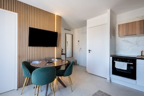 Una cocina moderna con horno empotrado, un área de comedor con una mesa redonda y sillas, y un televisor de pantalla plana montado en una pared de madera.