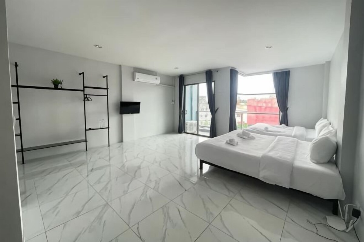 A modern hotel room with a large bed, a TV, a balcony with a view, and a white tiled floor.