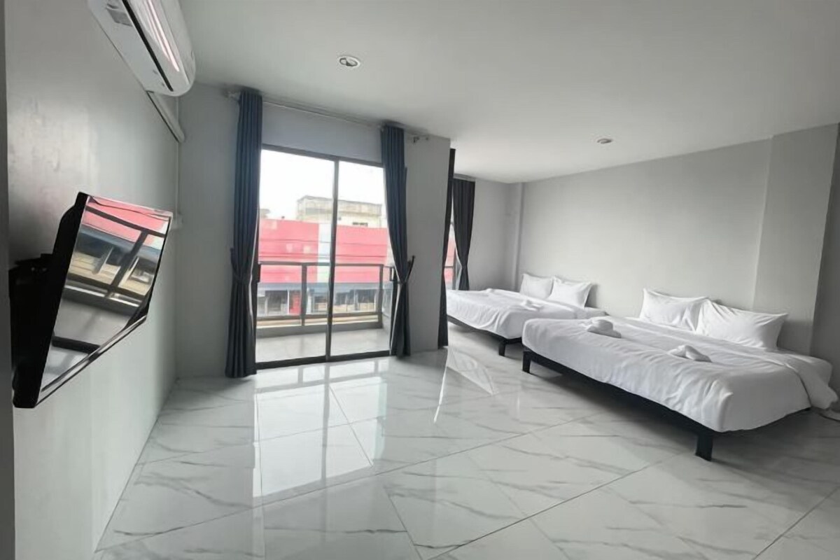 A hotel room with a large bed, a TV mounted on the wall, and a sliding glass door leading to a balcony.