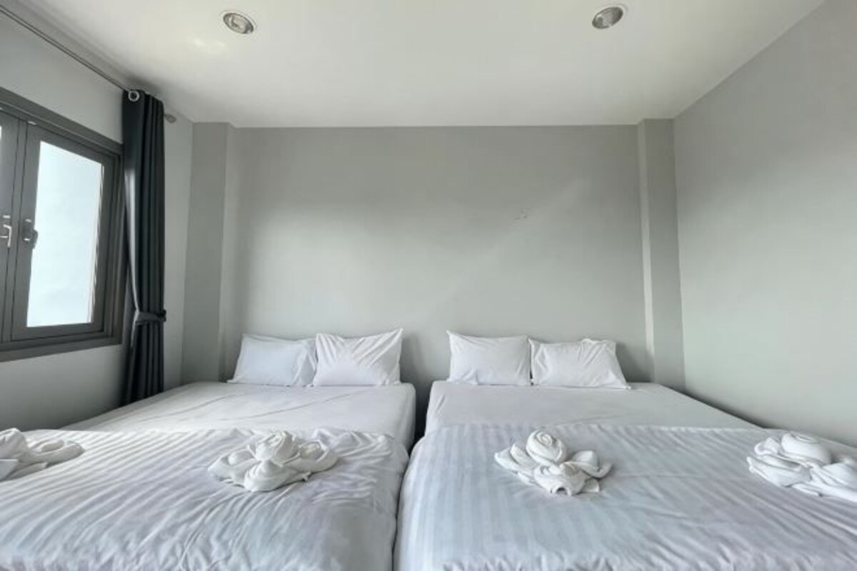 A hotel room with two beds, a large window, and a view of the sky.