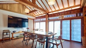 A spacious dining area with a long wooden table and chairs, a television mounted on the wall, and large sliding glass doors with a geometric pattern. - Traditional House Hotel Andong Villa (Andong-si)