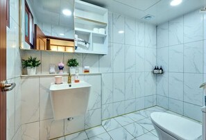A modern bathroom with a marble floor, a white sink, and a toilet. There are shelves above the sink with toiletries and a mirror. - Traditional House Hotel Andong Villa (Andong-si)