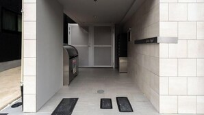 A narrow hallway with a trash bin, a door, and a sign on the wall. - Apiche Oji (Tokyo)