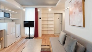 A modern living room with a sofa, a flat-screen TV, and a kitchen area with white cabinets and a microwave. - Apiche Oji (Tokyo)