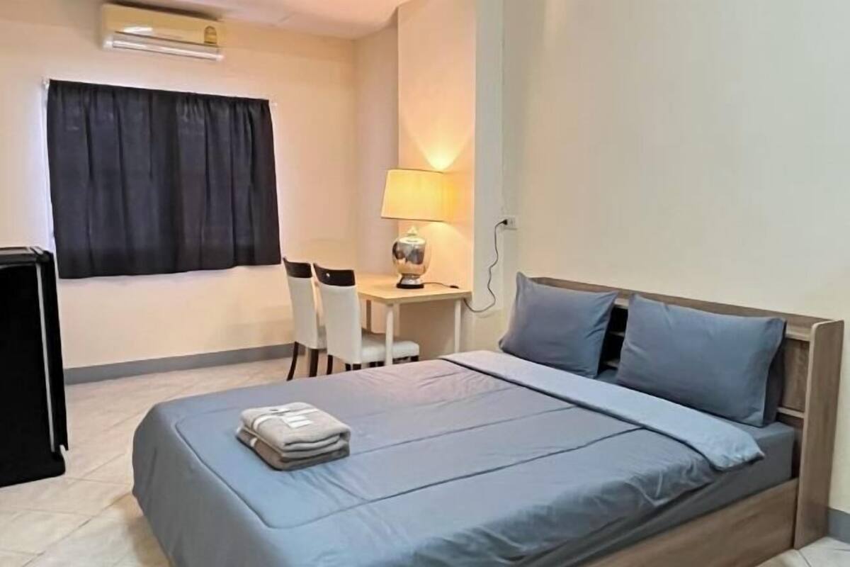 A hotel room with a bed, a desk, a chair, a lamp, and a TV.