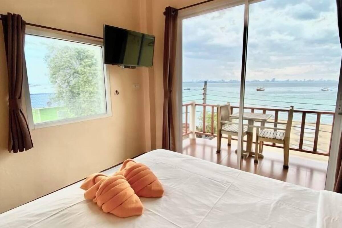 A room with a bed, a TV mounted on the wall, and a balcony with a view of the sea.