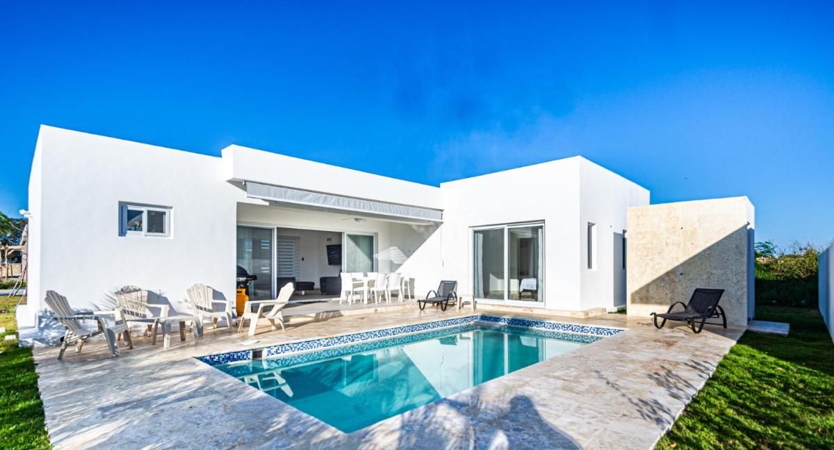 A modern house with a swimming pool, outdoor seating, and a clear blue sky.