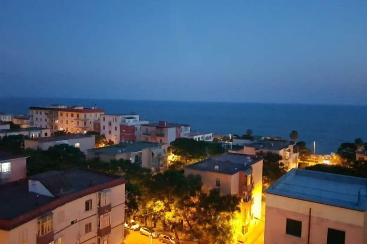 A coastal town at dusk with buildings and a street illuminated by streetlights.