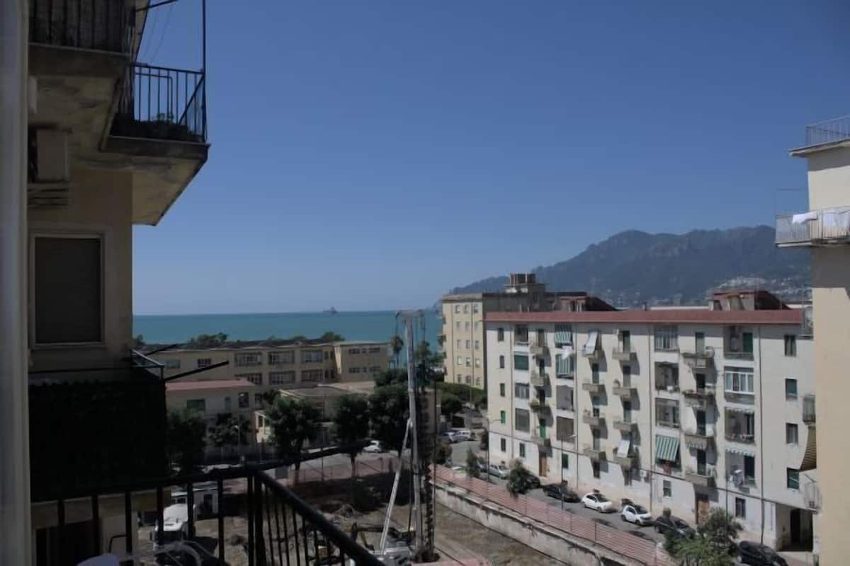 A residential building with balconies, a clear view of the sea, and a mountainous backdrop.