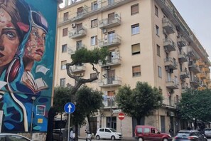 Un immeuble résidentiel à plusieurs étages, doté de balcons, avec un panneau de signalisation et des voitures garées dans la rue.
