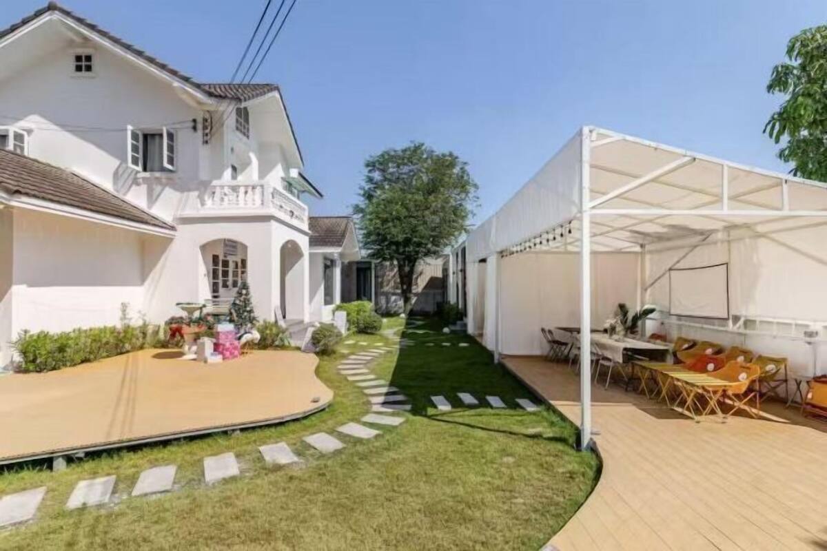 A white house with a covered patio, a lawn, and a white tent structure.